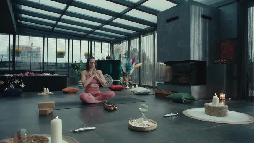 Woman sitting on the floor practicing yoga and meditating with candles and incense on the floor