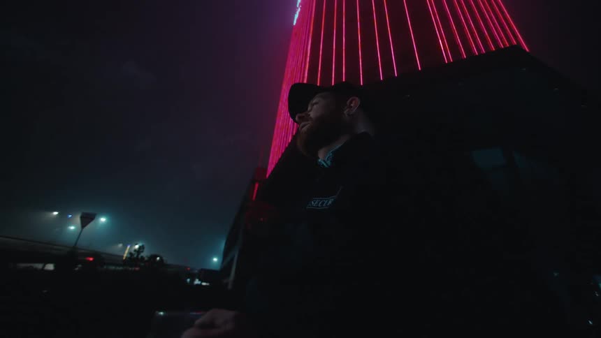 A man stands outside in the dark smoking a cigarette and drinking from a mug