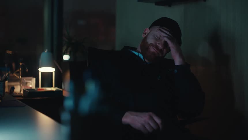 Desk lamp glows in the darkness as a security guard sits in a chair falling asleep