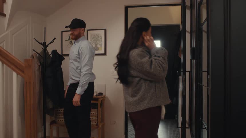 A man enters his own and kisses a woman on her cheek as she looks in a mirror