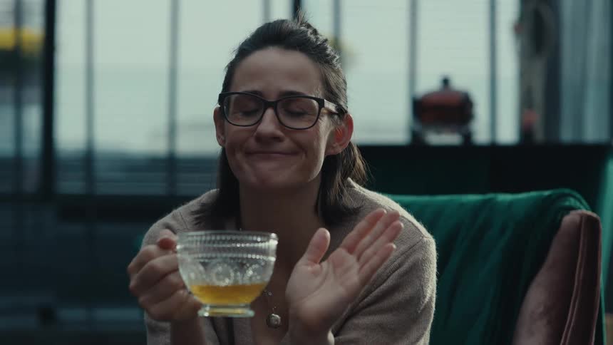 Woman wearing glasses holds a cup and talks in an indoor setting