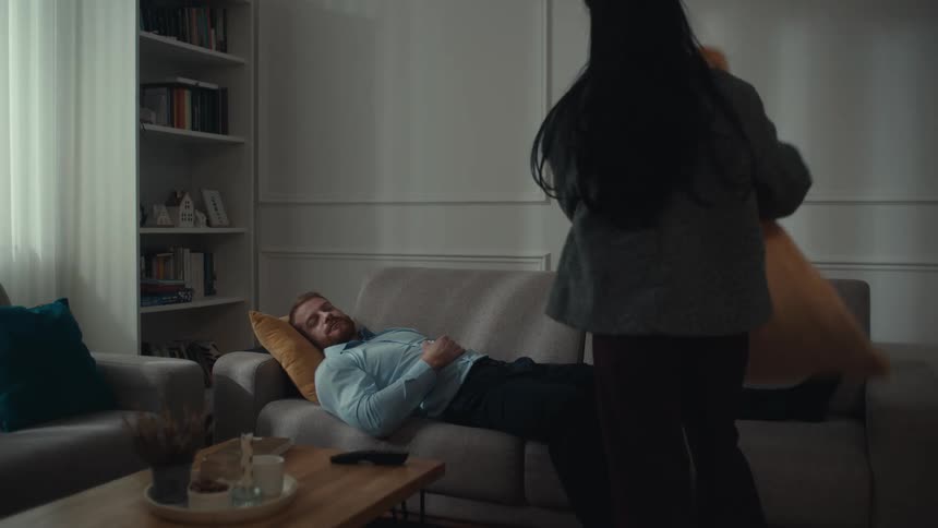 The woman lays a blanket on the man sleeping on the couch