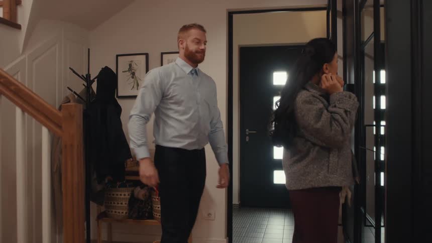 A man enters a home and removes his jacket as a woman prepares to leave