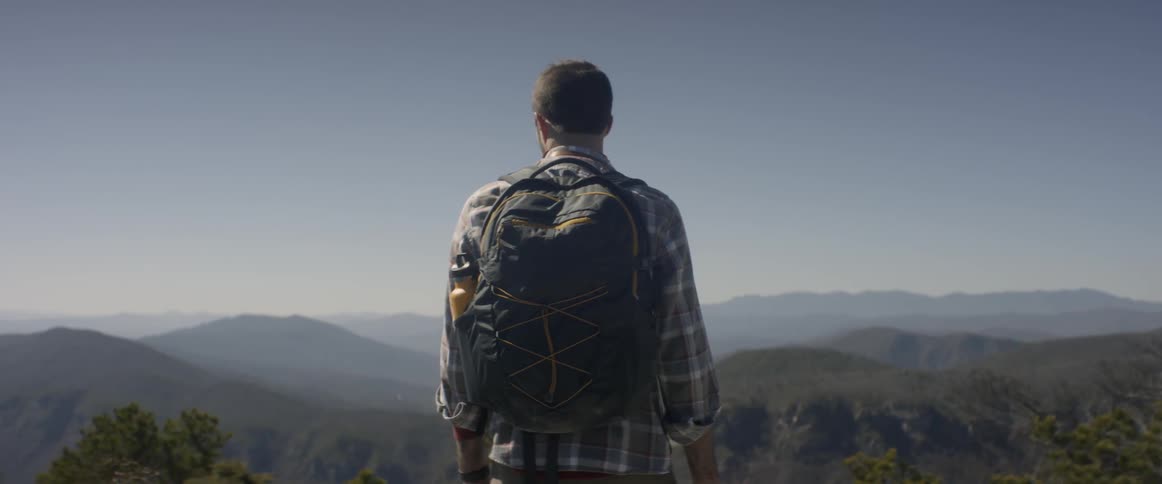 A hiker stands atop a mountain with a backpack