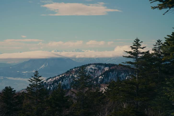 Mountain range with snowcovered areas and conifer forest under a partly cloudy sky