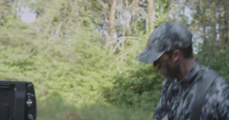 A hunter in camo picks up a crossbow and closes the truck tailgate