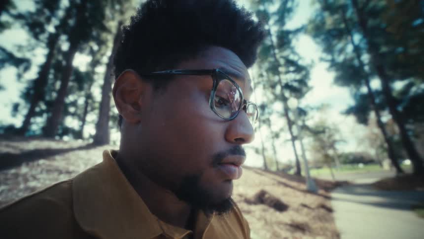 Man uses a smartphone in a park with trees and sunlight in the background