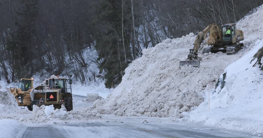Heavy machinery removes a large volume of accumulated snow along a roadside in a forested area
