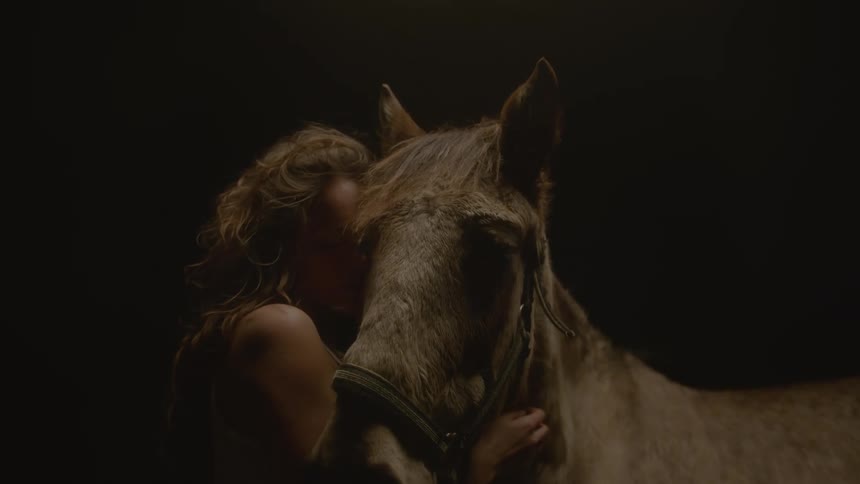 Woman holds a horses head under low lighting in a dark setting