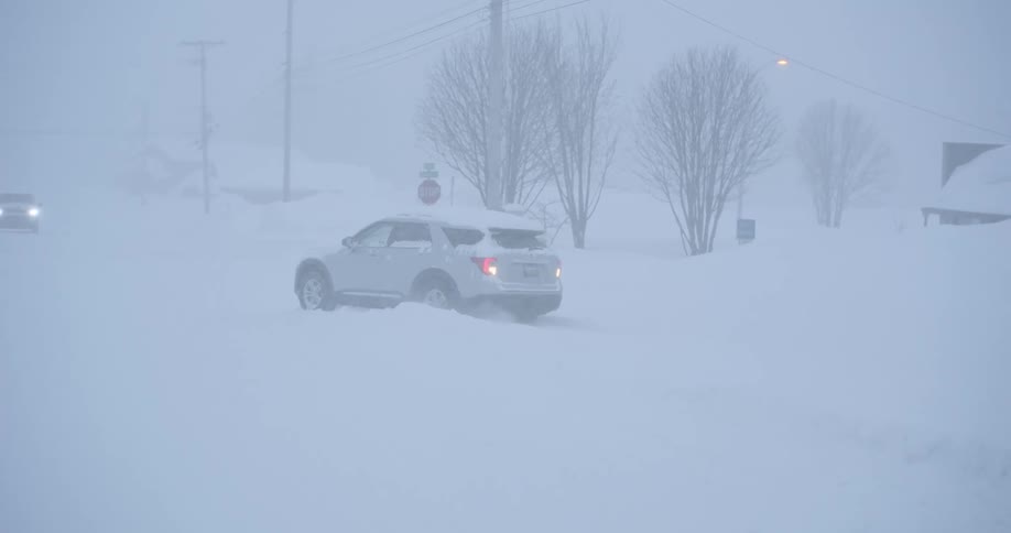 A silver suv maneuvers through deep snow on a street during a heavy blizzard