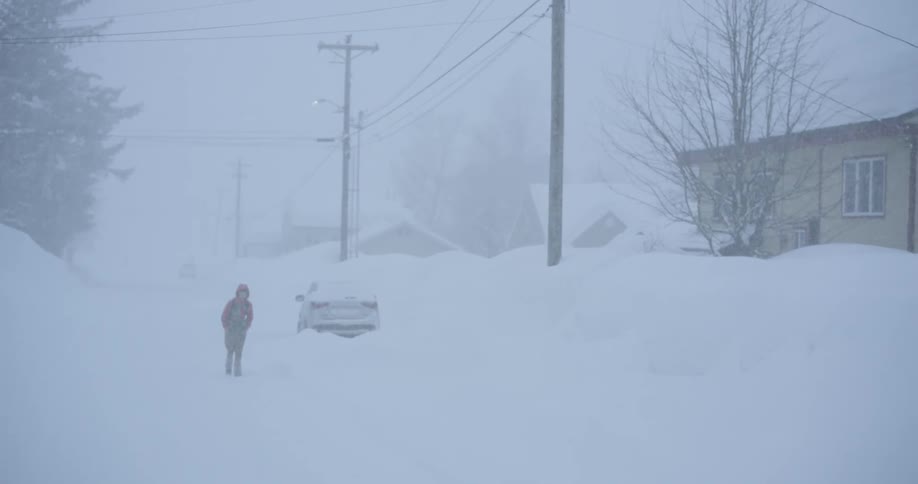 Person walks along a residential street covered by heavy snow during a blizzard