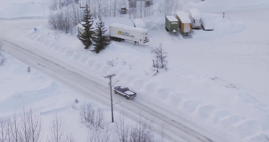 A pickup truck drives through a snow covered rural intersection in a quiet winter town