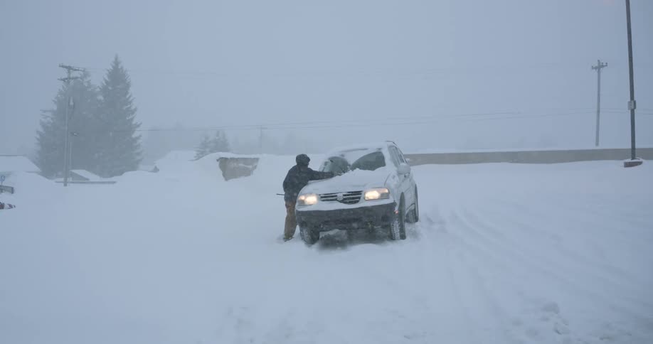 A person is standing next to a vehicle that is stuck in snow on a road