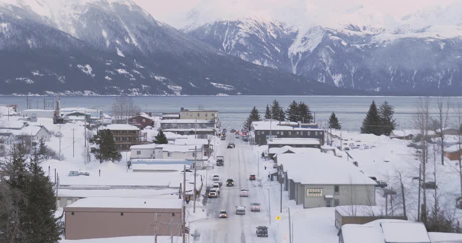 Snowcovered town with a main road leading toward a lake and mountains in the background