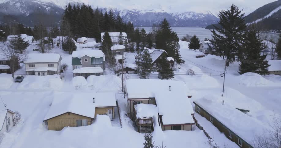 Residential area covered in snow with houses trees and mountains in the background