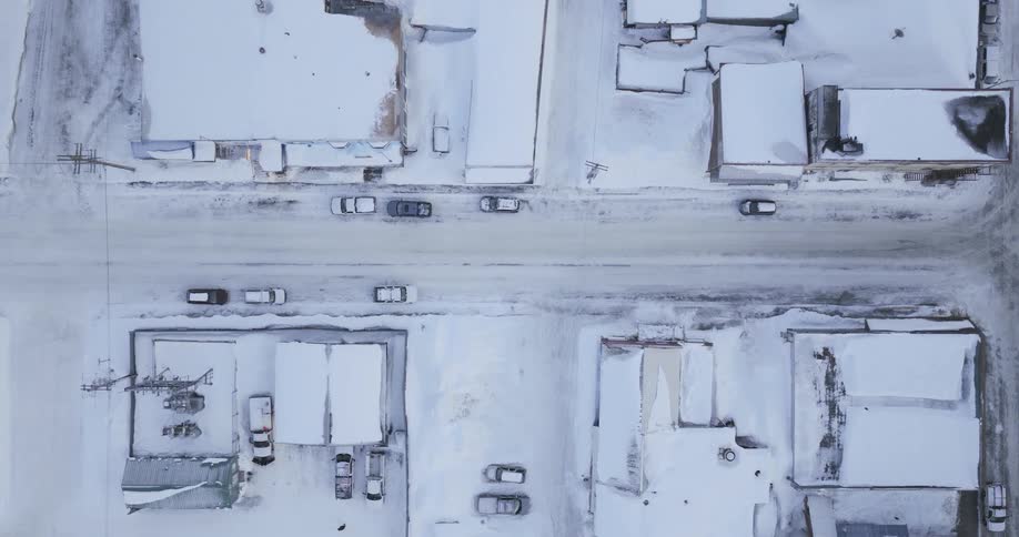 A top down aerial view shows a town where snow covers the roofs of buildings and the streets