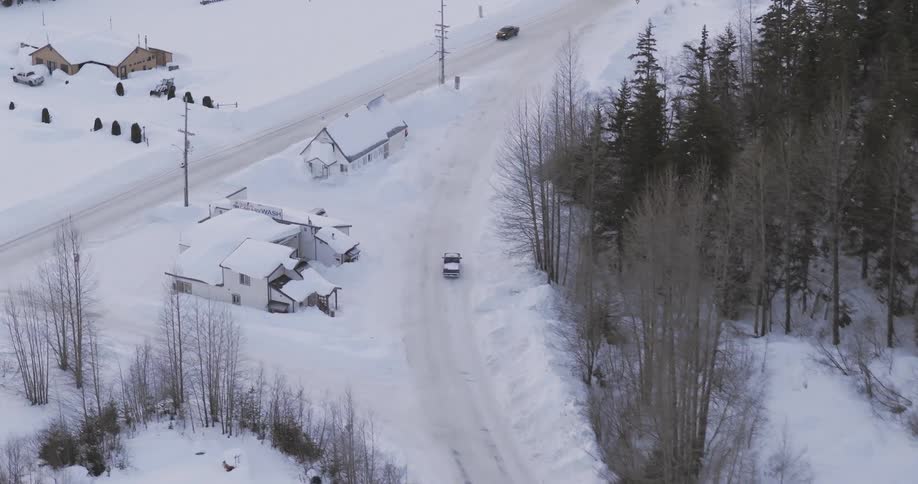 Aerial view shows a snowcovered road with vehicles moving between houses and a wooded area