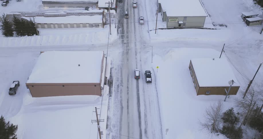 Vehicles travel towards and from the water on a road leading through a coastal town on a snowy winter day