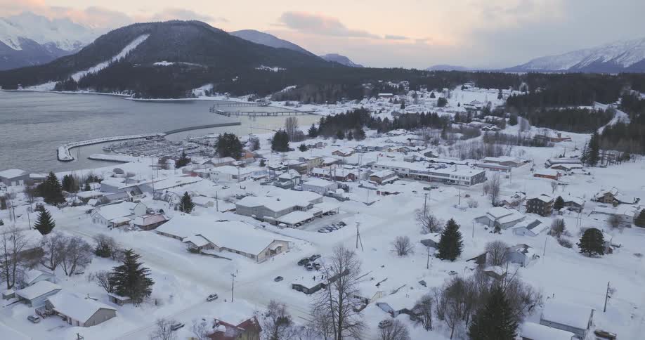 Snow covered town stands on the coast near forests and mountains on a winter day