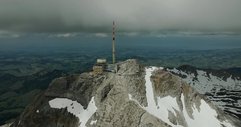 Telecommunications structure installed on the summit of a rocky mountain with remaining snow and dense clouds