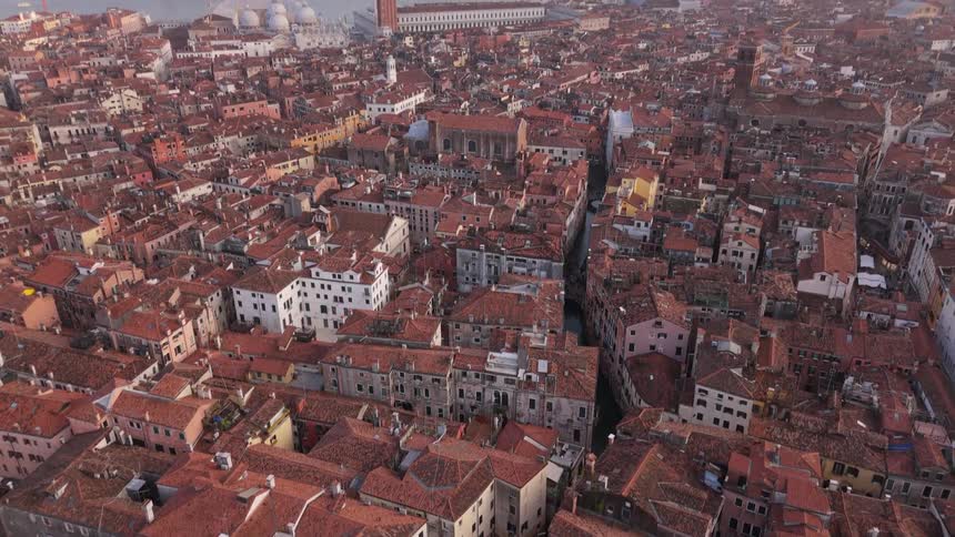 Aerial view of a historic city with terracotta rooftops and towers by a lagoon
