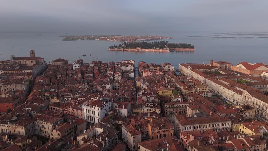 Aerial view of a historic city with terracotta rooftops by a lagoon with islands in the background