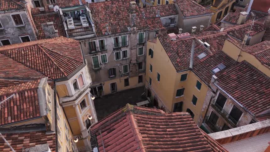 An aerial view shows a narrow courtyard surrounded by several tall buildings with orange tile roofs