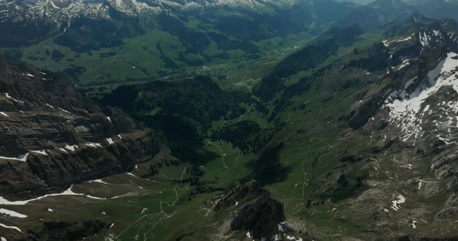 A mountain range has snow on the peaks and green grass in the valley