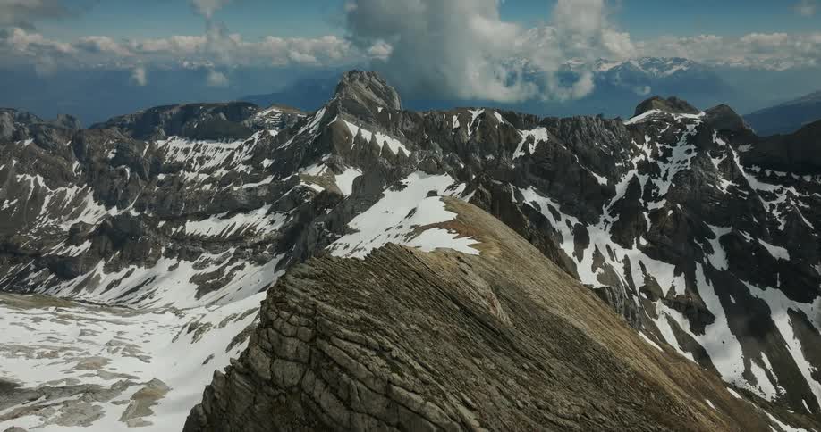 Moving over peaks of a mountain ridge with mountains in the distance and snow on the rough terrain