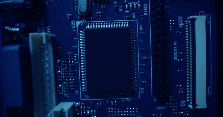 A slow rotating macro shot explores the intricate landscape of a blue computer circuit board highlighting its central microchip and complex electronic pathways
