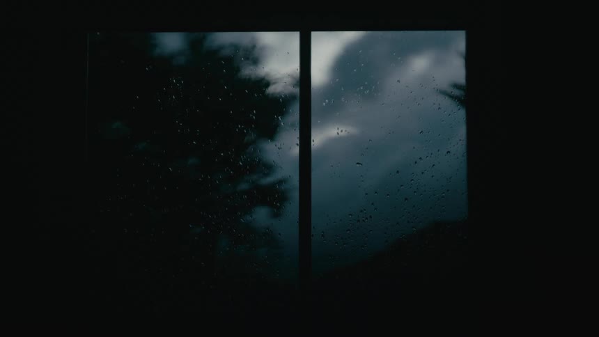 Raindrops run down a window with a cloudy sky visible in the background