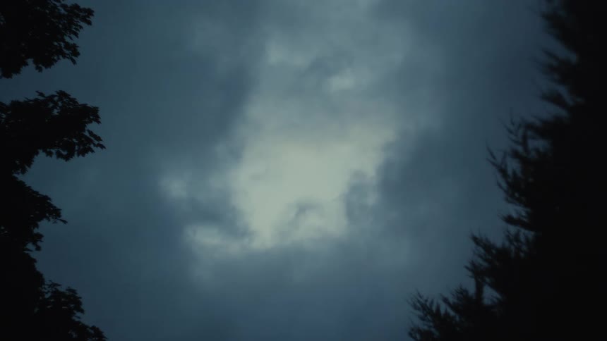 A low angle shot captures a dark and moody sky filled with thick grey clouds moving slowly