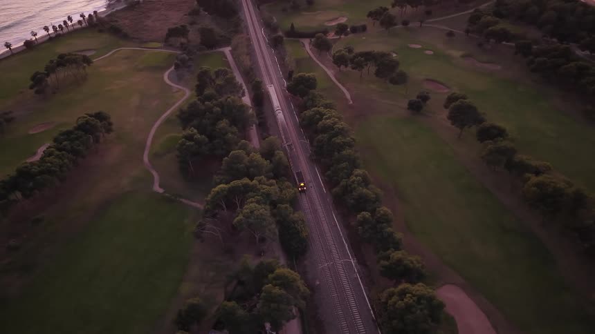 Aerial view of a train traveling along coastal tracks through green landscape at sunset
