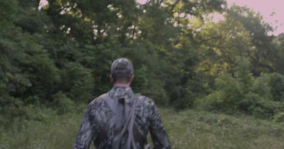 A man hikes in the grass carrying equipment