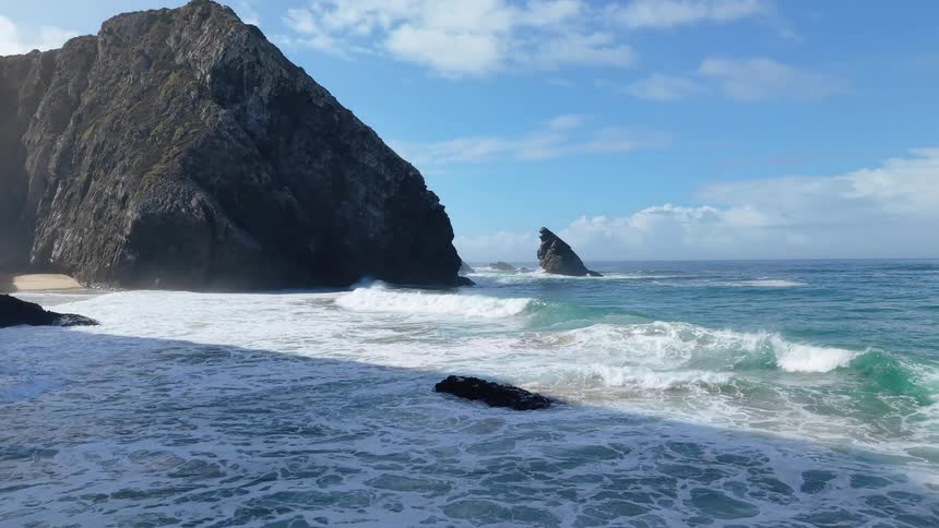 Waves are crashing onto a beach and against the cliffs