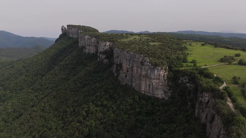 Field and road on a forested mountaintop with stone cliffs along the edge