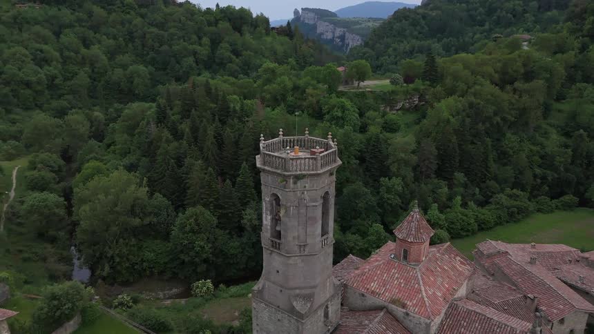 Aerial view of a historic stone tower rising above a hillside village surrounded by dense forest