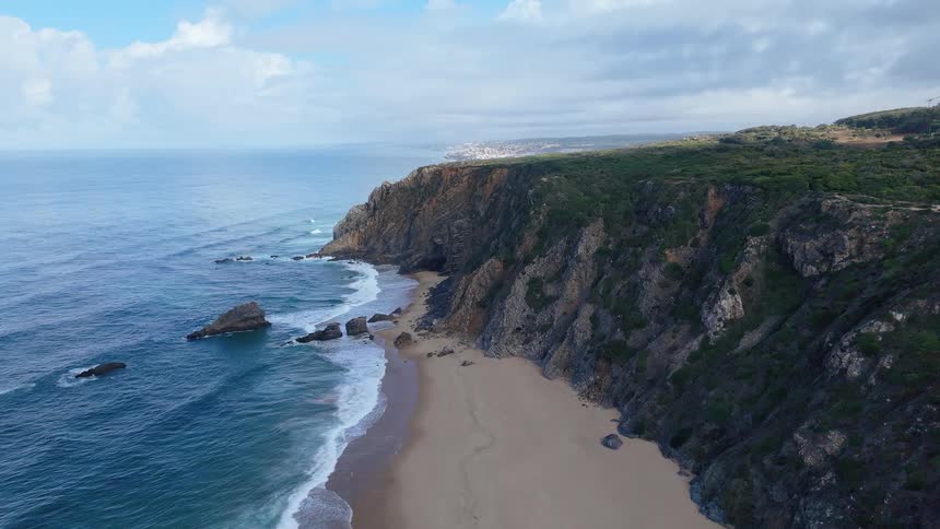 Aerial view of rugged coastal cliffs beside a sandy beach with waves crashing onto the shore
