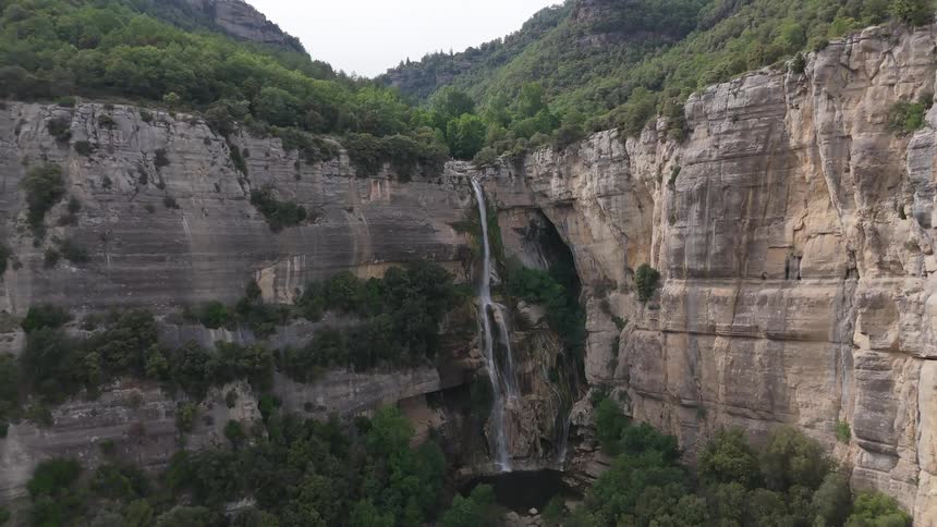Waterfall descends through rocky cliffs amid dense vegetation in a canyon