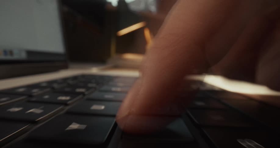 A close up low angle shot shows a person typing quickly on a black laptop keyboard resting on a wooden desk