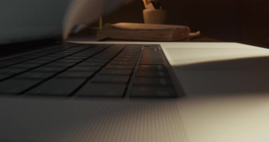 A hand closes a laptop on a desk in a dimly lit workspace