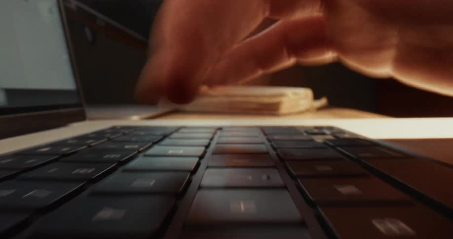 A close up view shows a person typing quickly on a laptop keyboard
