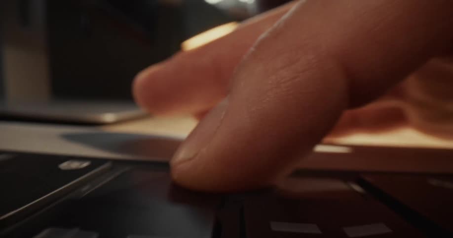 A man types on a black laptop keyboard at a wooden desk under warm light