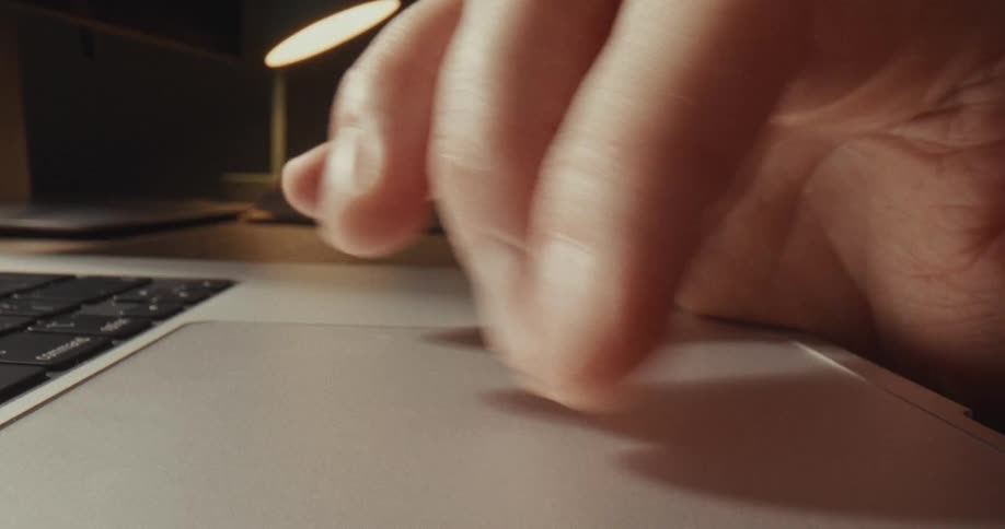 A close up view shows a person using a laptop trackpad