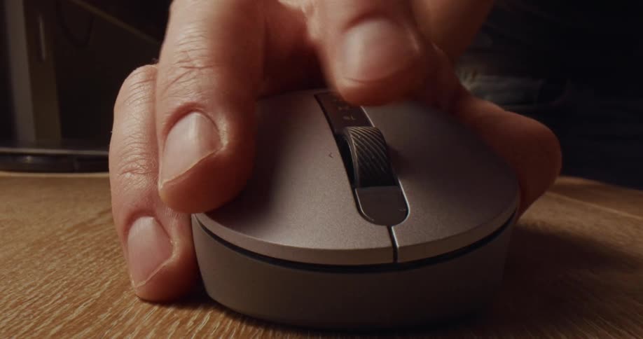 A close up view shows a person using a computer mouse on a wooden desk