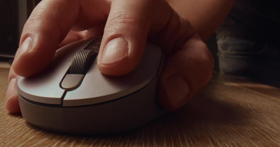 A closeup shot of a persons hand using a modern circular computer mouse on a wooden surface the person is shown clicking the buttons and navigating with the scroll wheel in a series of quick deliberate movements