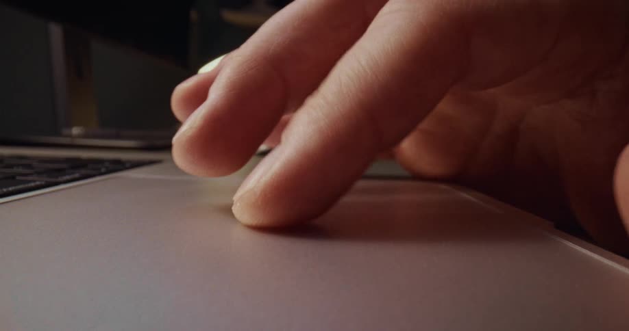 A close up view shows a person using a touch pad on a laptop