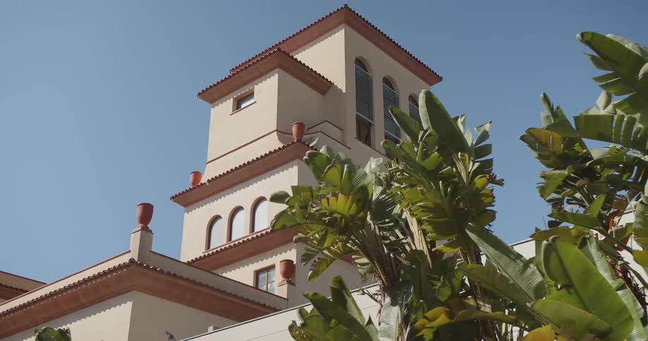 Building tower with tiled roof and arched windows among palm trees under a blue sky