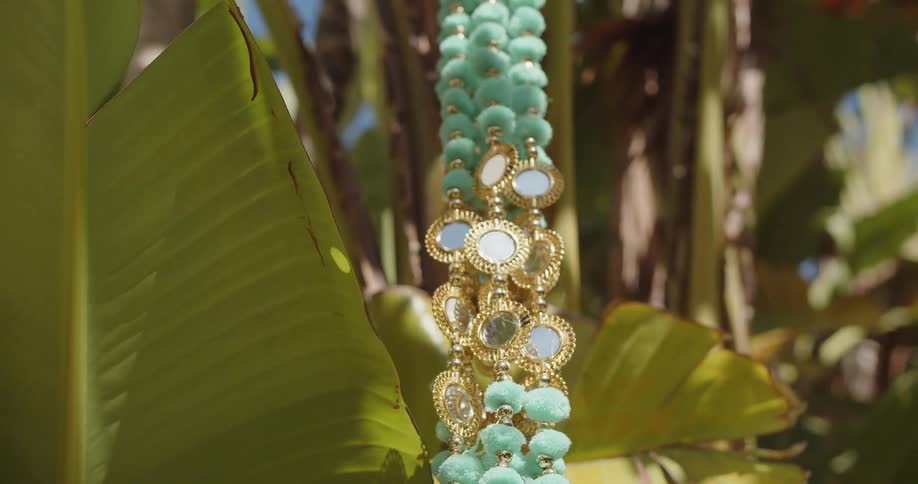A close up view shows a decorative garland with light green pom poms and gold accents hanging from a tropical tree