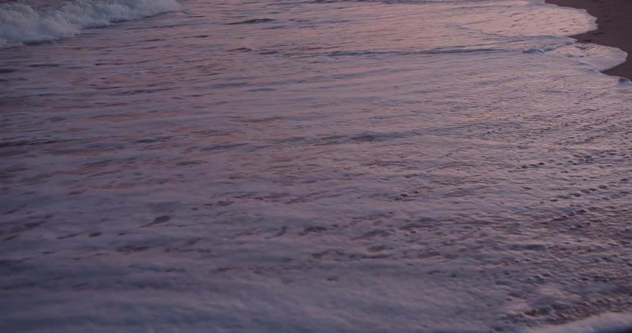 Ocean waves reaching the sandy shoreline at dusk